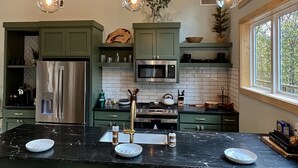 A modern kitchen with green cabinets, stainless steel appliances, and a black marble countertop. - The Fir - 2 Bedroom Cabin (Broken Bow)