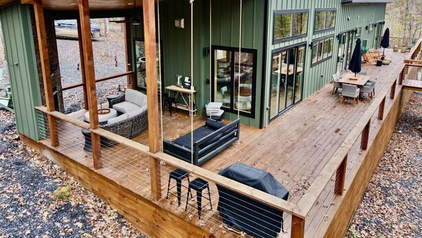 A wooden deck with outdoor seating, a covered patio area, and large windows. - The Fir - 2 Bedroom Cabin (Broken Bow)