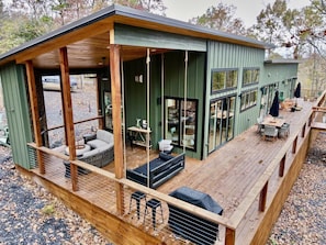 Terraza de madera con mobiliario exterior, un porche cubierto y amplios ventanales.