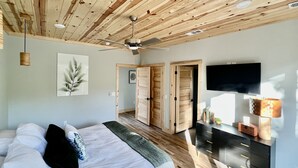 A bedroom with a wooden ceiling, a bed with pillows, a bedside table with a lamp, and a TV mounted on the wall. - The Fir - 2 Bedroom Cabin (Broken Bow)