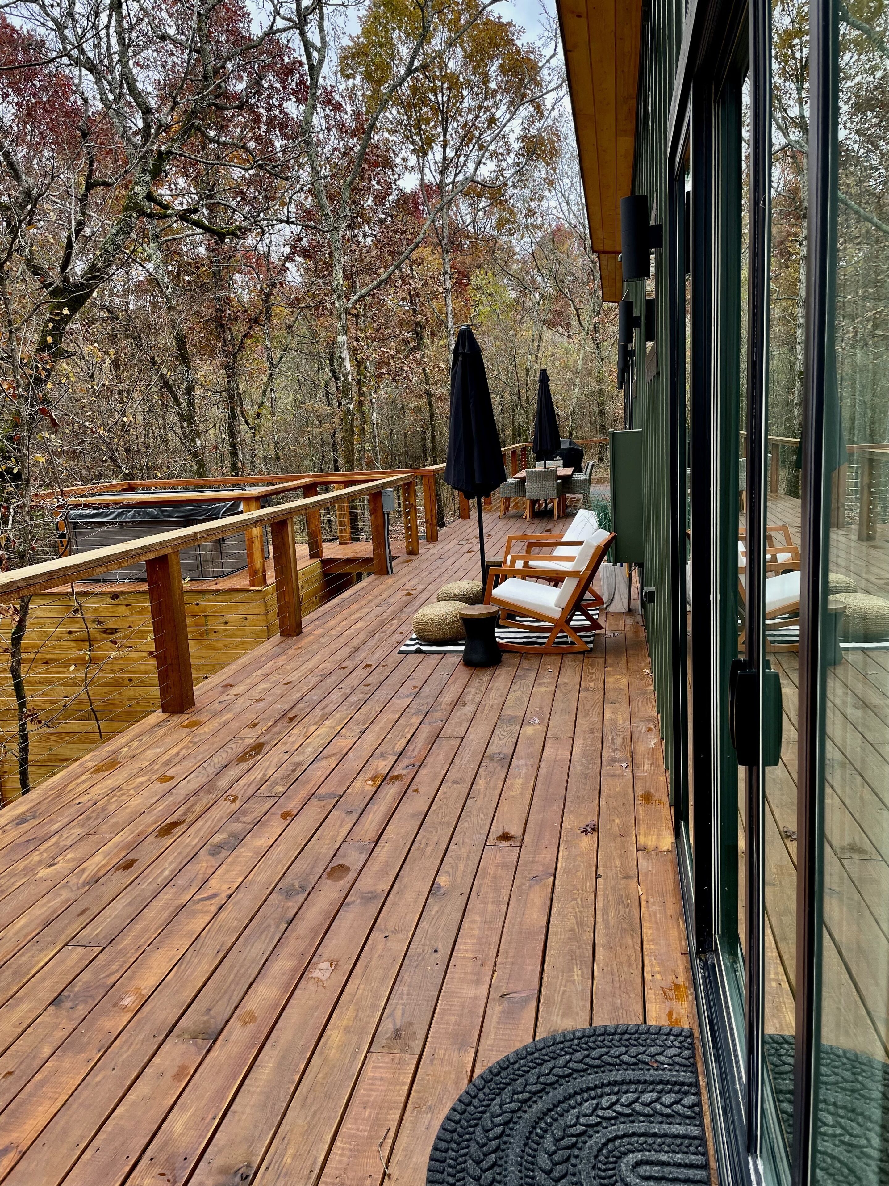 Une terrasse en bois, aménagée avec du mobilier d’extérieur, notamment des chaises et une table, et offrant une vue sur une zone boisée.