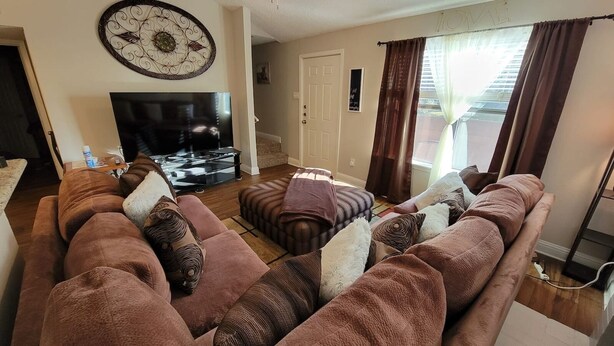 A living room with a brown sofa set, a flat-screen TV, and a decorative wall piece.