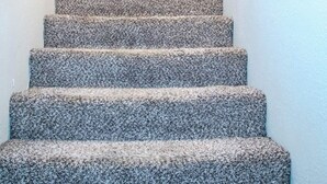 A carpeted staircase with a handrail on the left, a picture of a tiger on the wall, and a door at the top.
