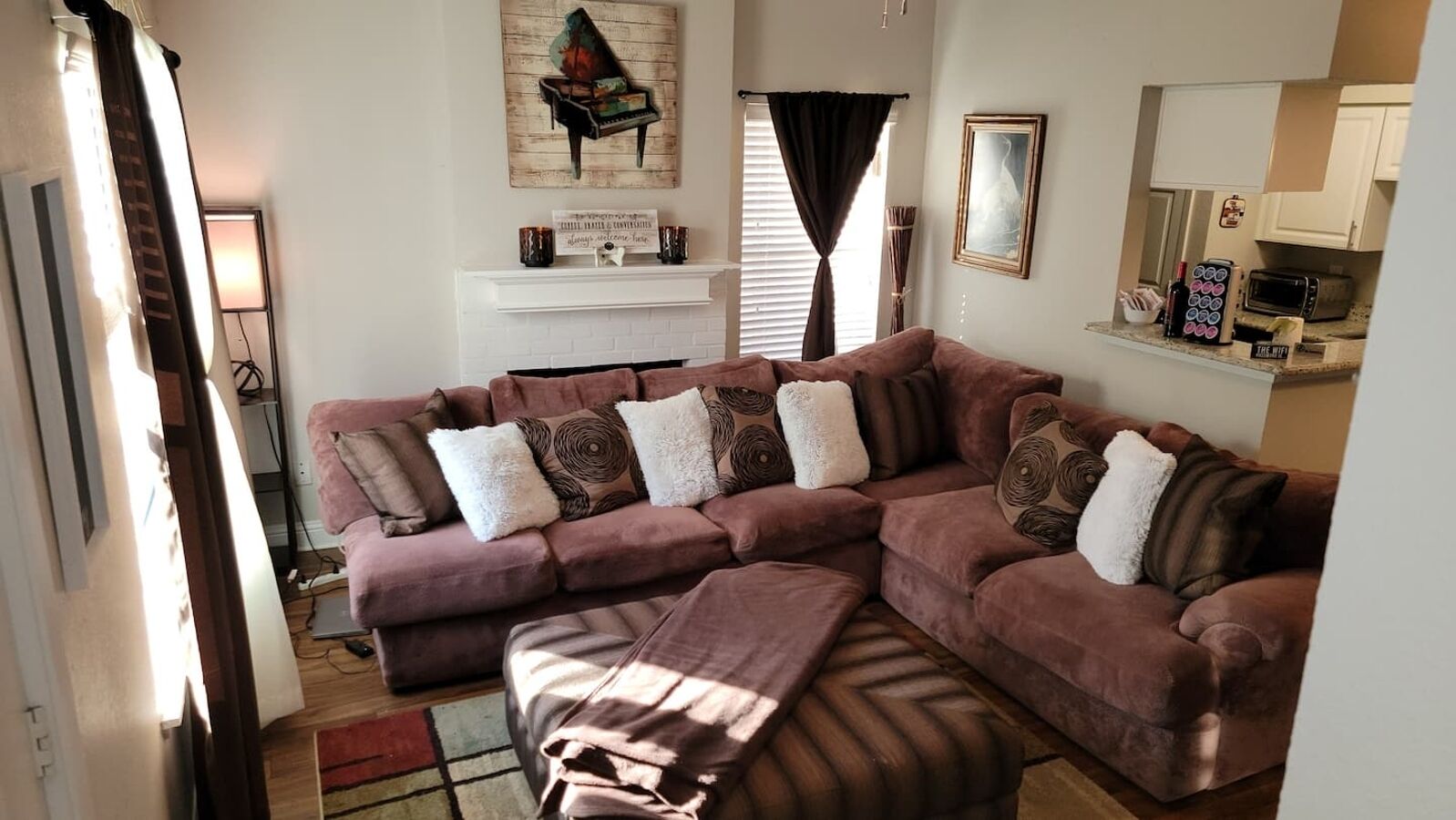 A living room with a sectional sofa, a fireplace, and a kitchen area visible in the background.
