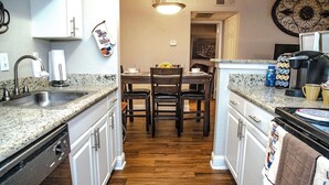 A kitchen with granite countertops, white cabinets, a wooden dining table, and a hanging kitchen towel.