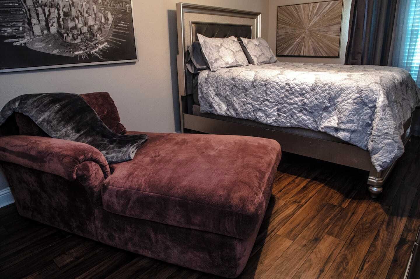 Un dormitorio con una cama, un chaise lounge y un cuadro grande en la pared.