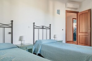 Un dormitorio con dos camas, cada una con una colcha azul estampada, una mesita de noche con lámpara y un armario de madera.