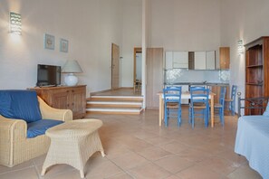 Una sala de estar con un sofá, una mesita y un televisor. Hay una zona de cocina con una mesa de comedor y sillas.