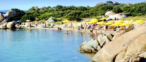A beach with clear water, rocks, and people.