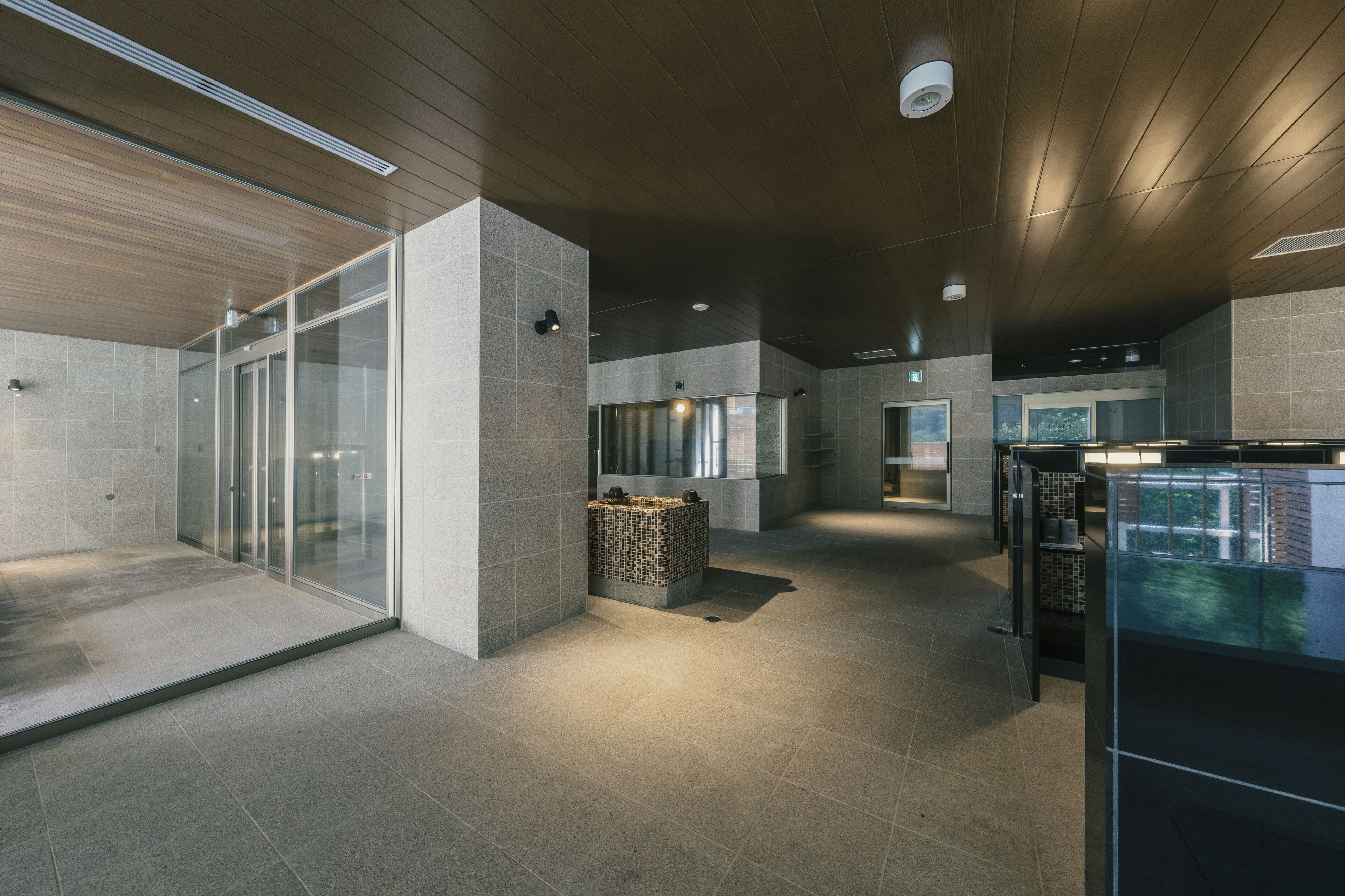 A modern interior with a glass partition, a tiled floor, and a wooden ceiling.