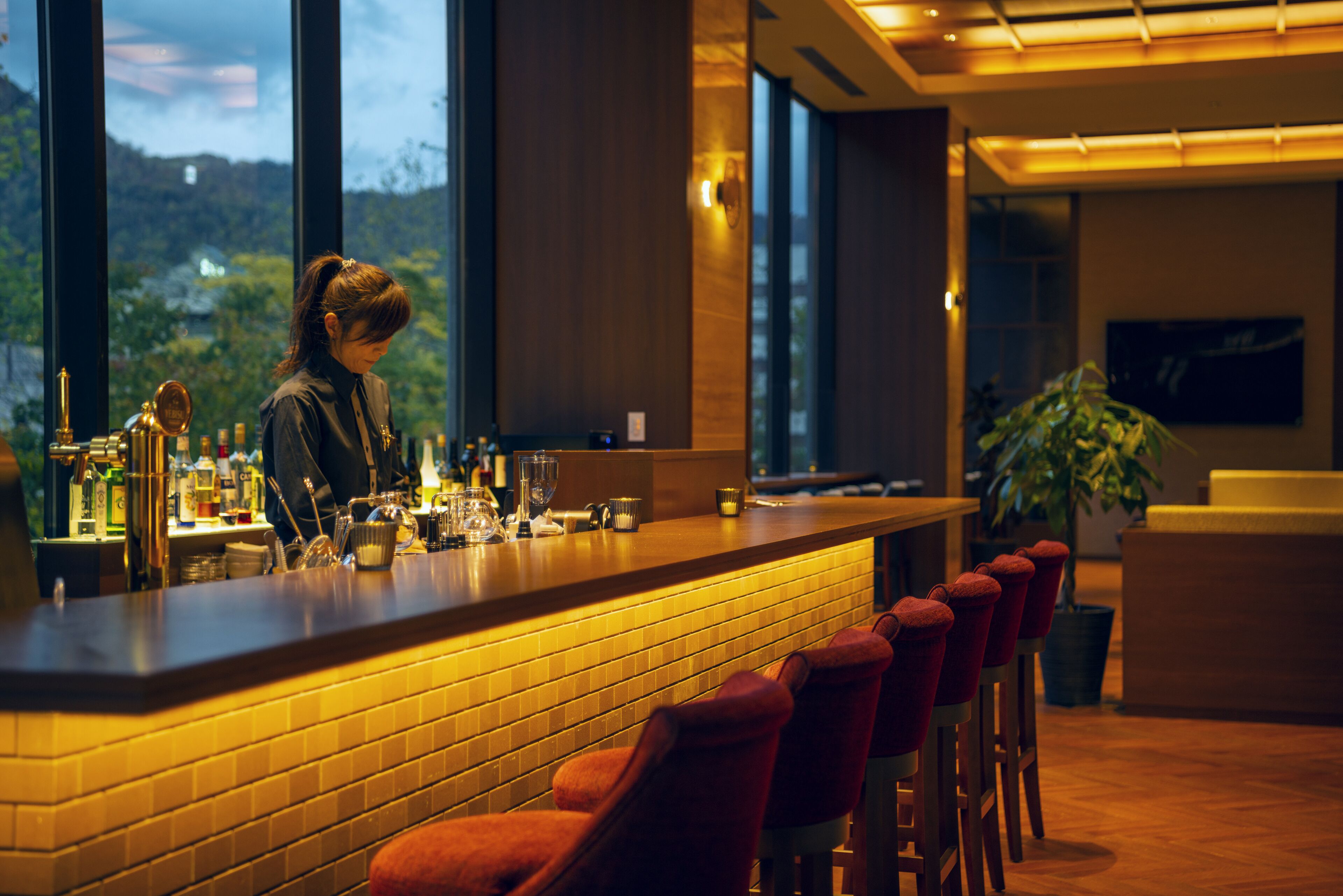 A bar area with a brick wall, red bar stools, and a bartender.