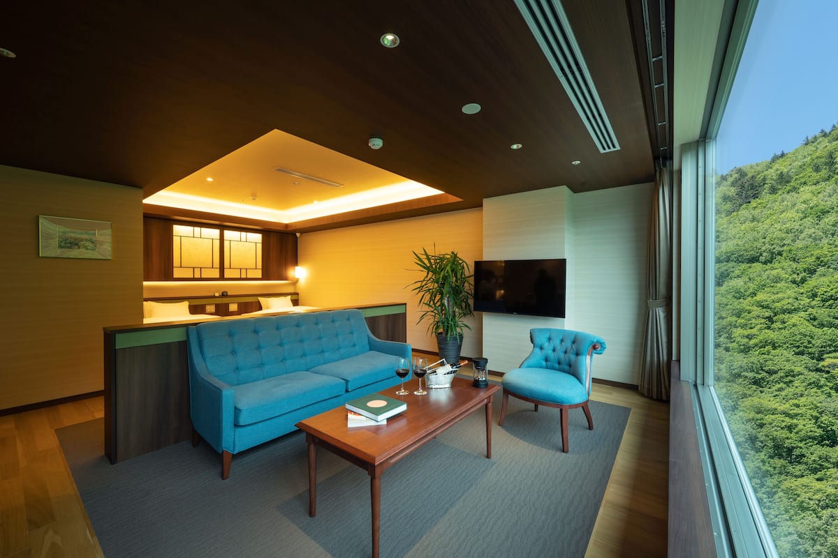 A modern living room with a blue sofa, a wooden coffee table, and a view of a green hillside through large windows.
