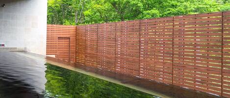 A swimming pool with a wooden fence and a view of lush greenery.