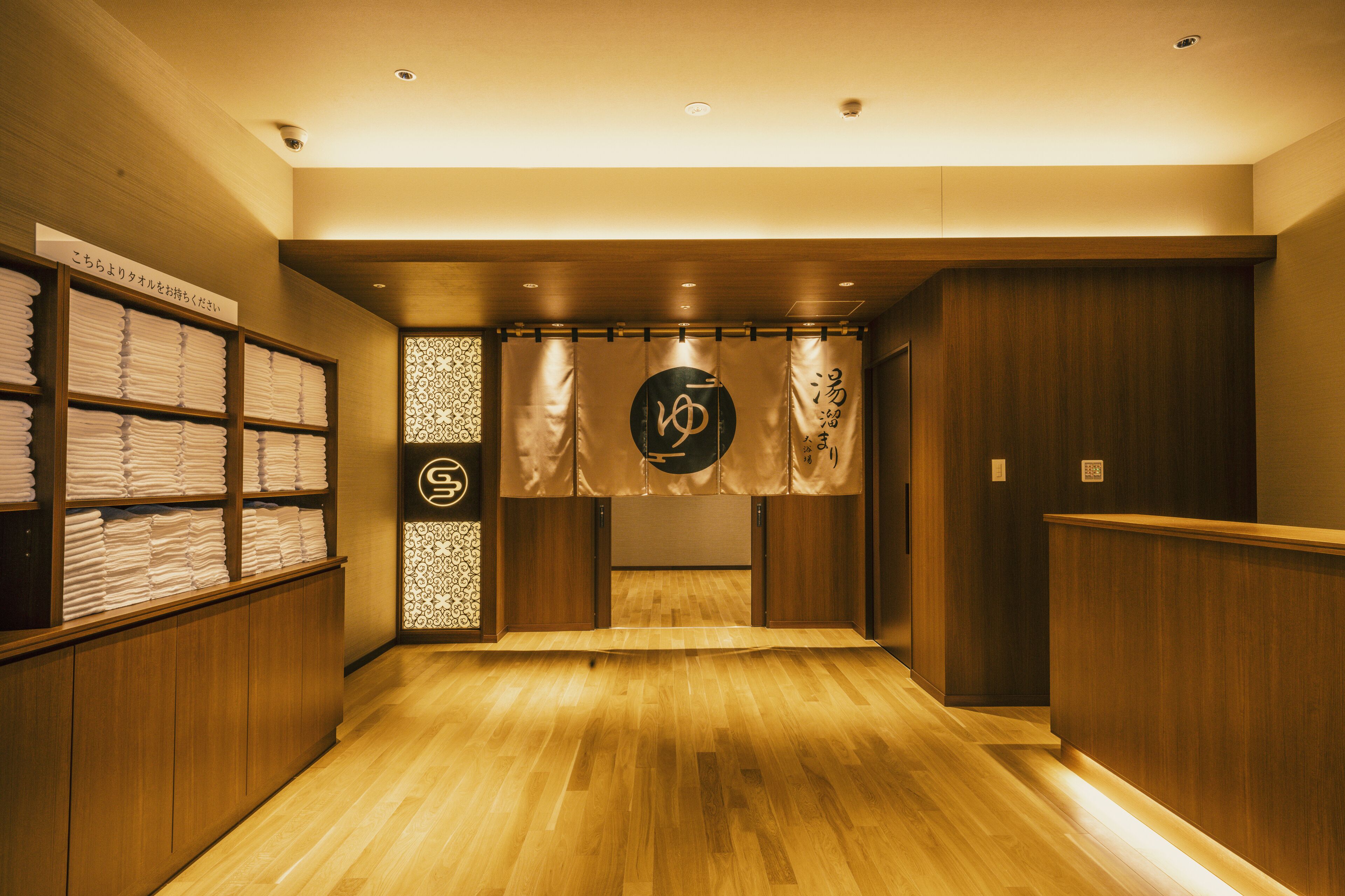 A hotel lobby with wooden flooring, a reception desk, and shelves with folded towels.