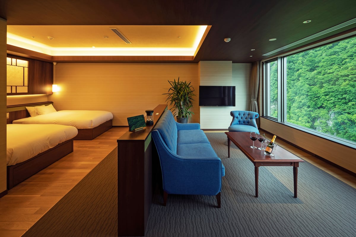 A hotel room with a large bed, a sofa, a coffee table, and a view of a forest.