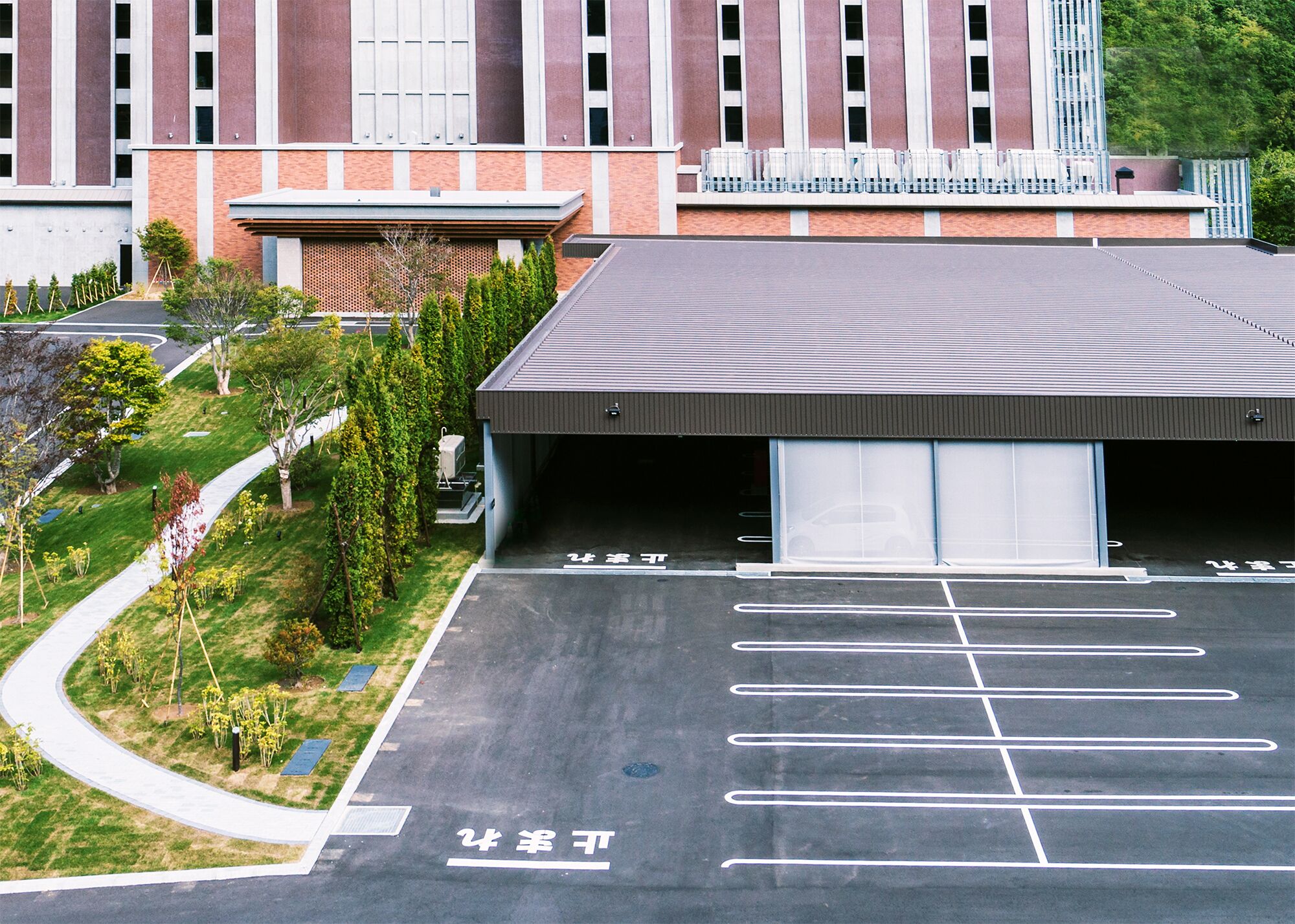 A parking garage with clear markings for parking spaces, a covered area, and a building with a brick facade in the background.