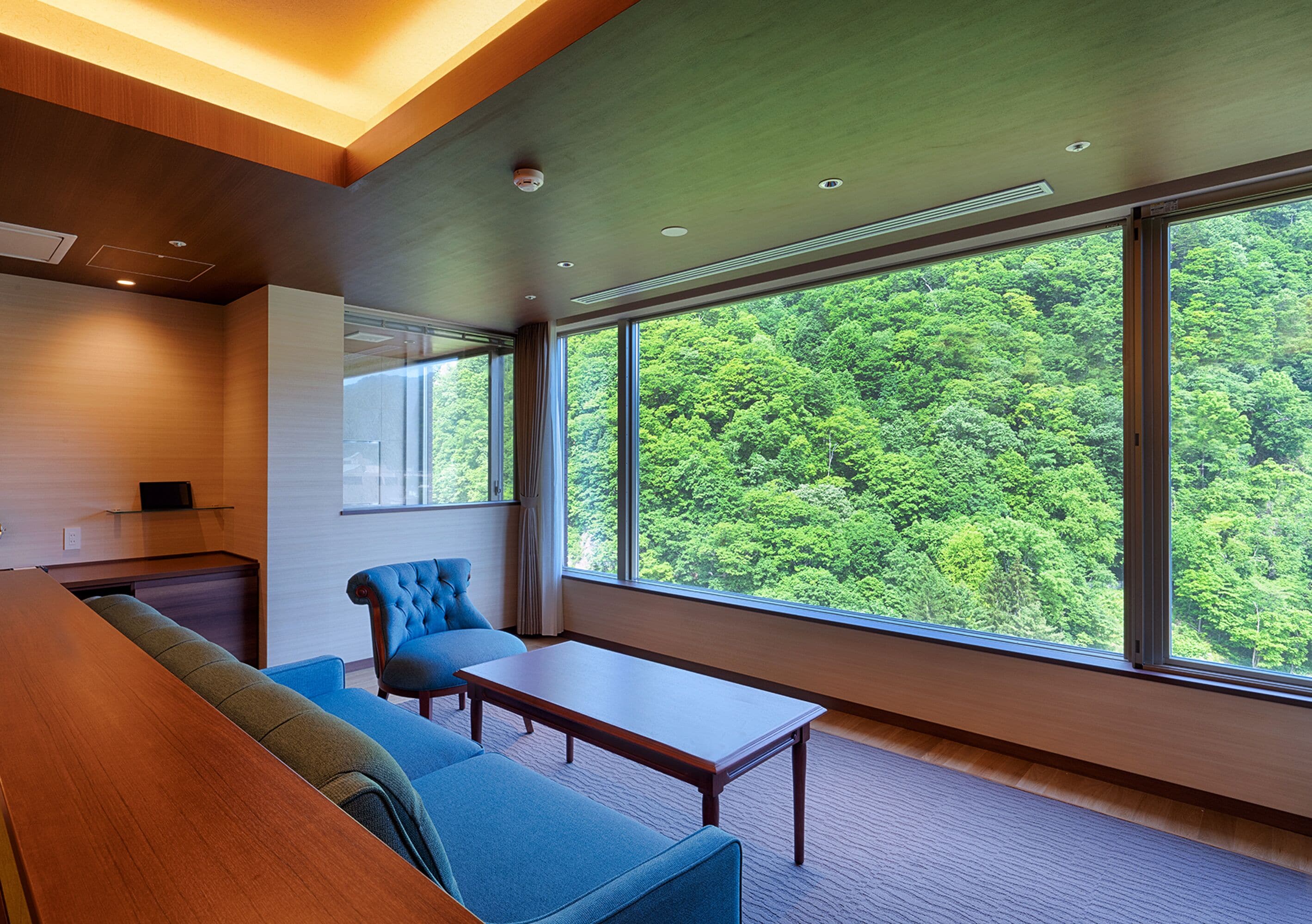 A modern room with a large window, a sofa, a table, and a desk.