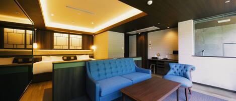 A modern hotel room with a blue sofa, a wooden coffee table, and a large window offering a view of the city.