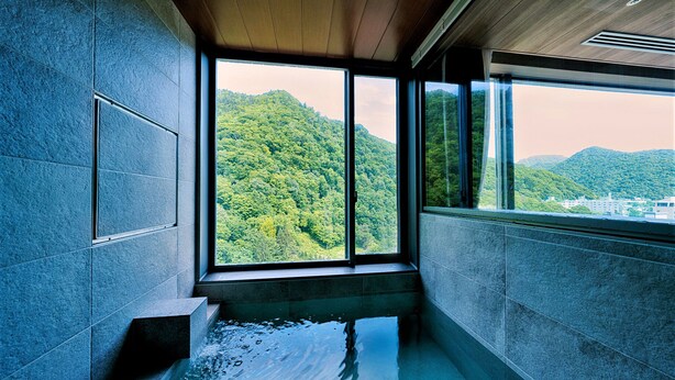 Un baño moderno con un amplio ventanal, techo de madera y vistas a una montaña boscosa.