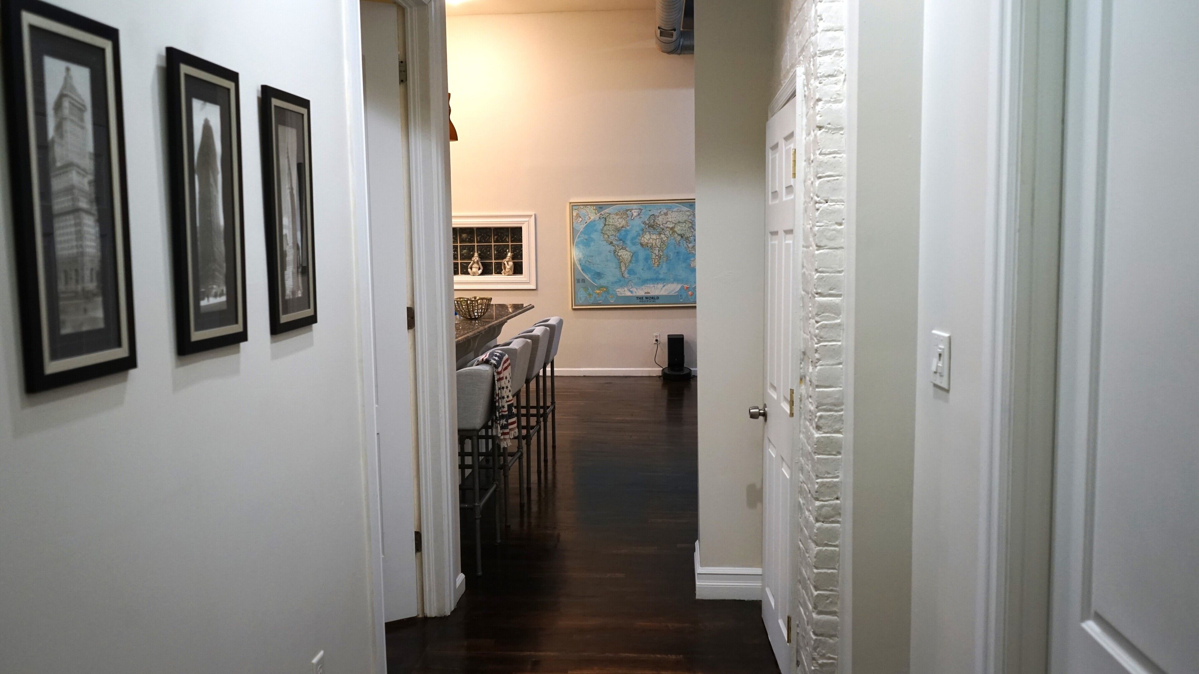 A hallway with framed pictures on the wall, a world map, and a dining area with chairs and a table.