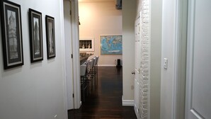 A hallway with framed pictures on the wall, a world map, and a dining area with chairs and a table.