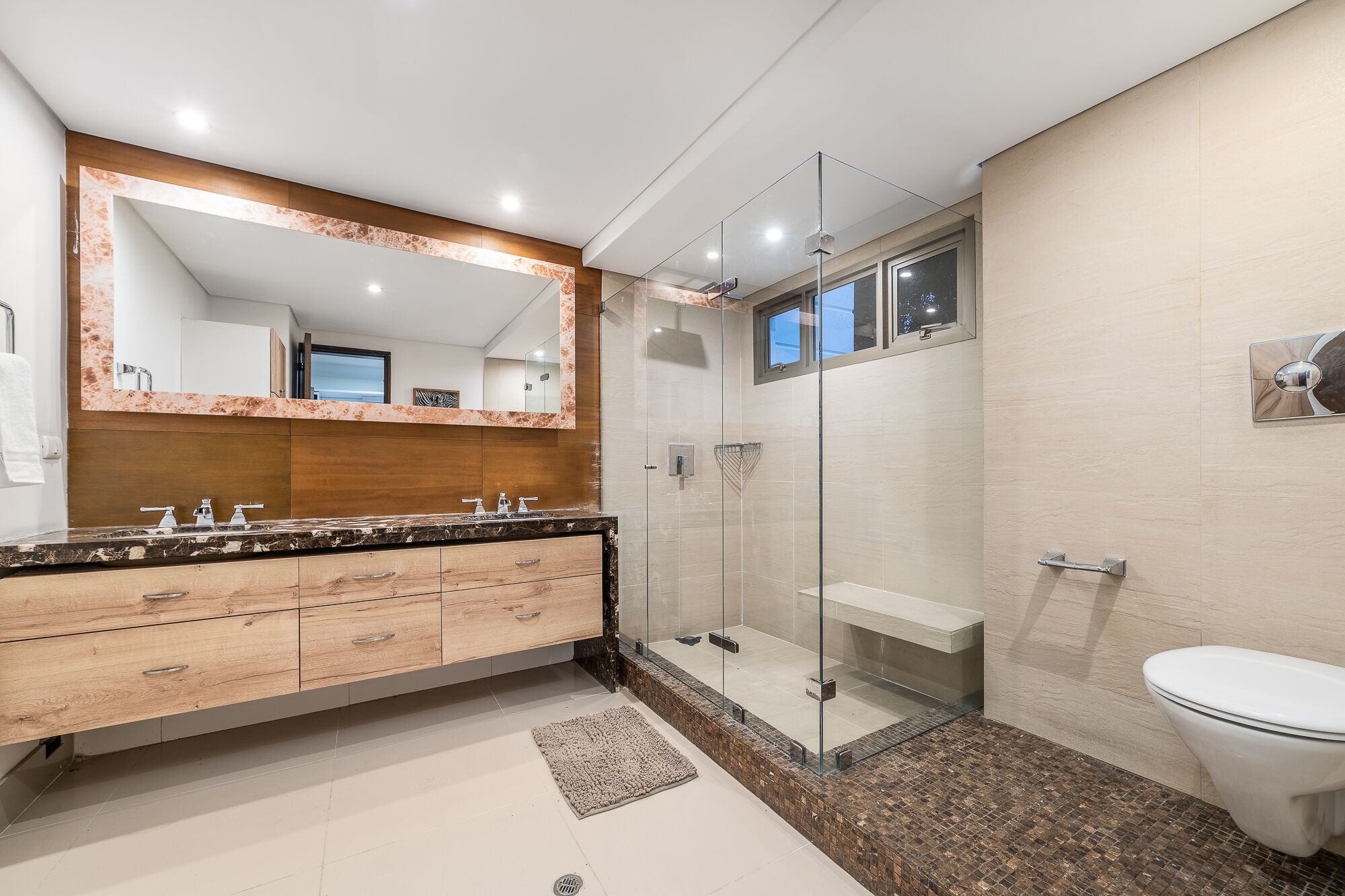 Une salle de bain moderne avec un meuble-lavabo en bois, une cabine de douche en verre et des toilettes blanches.
