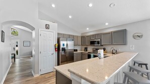 A modern kitchen with a central island, stainless steel appliances, and a view to the dining area. - **Luxury 4 bedroom Villa w/ pool in golf community, mins away from DisneyWorld** (Davenport)