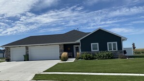 A two-story house with a dark green exterior, a white garage door, and a well-maintained lawn. - Spacious new home with a country feel. (Kearney)