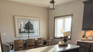 A kitchen with a central island, wooden chairs, a dining table, and a window with blinds. - Spacious new home with a country feel. (Kearney)