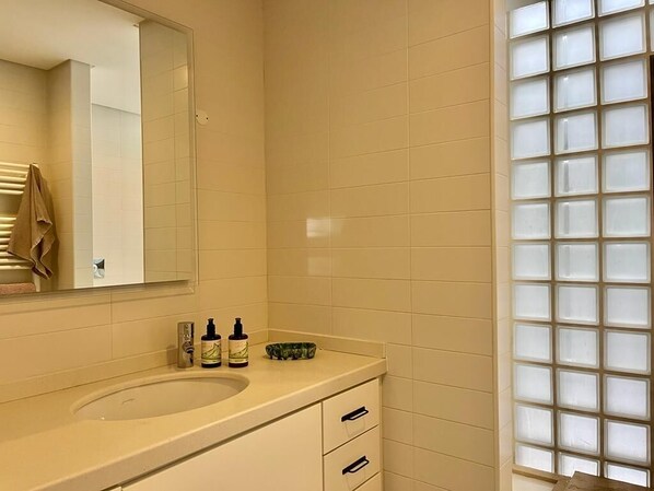 A bathroom with a beige sink, a mirror, and a window with frosted glass.