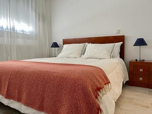 Una cama bien tendida con una manta roja, un cabecero de madera y dos lámparas de noche.