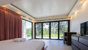 Een moderne slaapkamer met een groot bed, een flatscreen-tv en een glazen schuifdeur die uitkomt op een balkon met uitzicht op de omgeving.