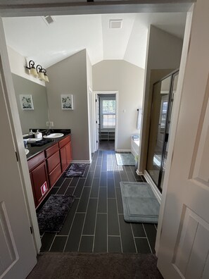 A hallway leading to a bathroom with a shower, a sink, and a mirror.
