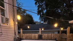 Un bain à remous doté d’une terrasse en bois et illuminé de guirlandes lumineuses, le tout entouré d’une clôture en bois.