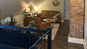 Un salon de style industriel, avec un canapé en cuir marron, une table basse ronde et un escalier doté d’une rampe en métal.