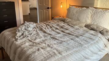 A bedroom with a large bed, a bedside lamp, and a door leading to a kitchen.