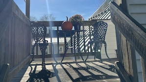Une terrasse en bois avec une pergola, une table entourée de chaises et une citrouille posée sur la table.