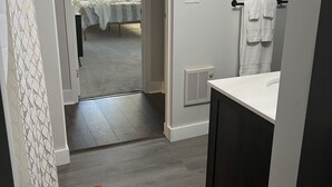Un couloir menant à une chambre avec un lit, une salle de bain avec un lavabo et des serviettes, et un tapis à motifs.