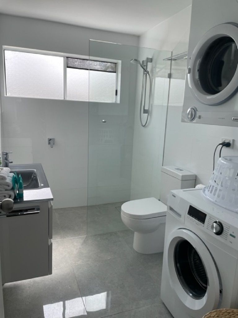 A modern bathroom with a washing machine, toilet, and shower.