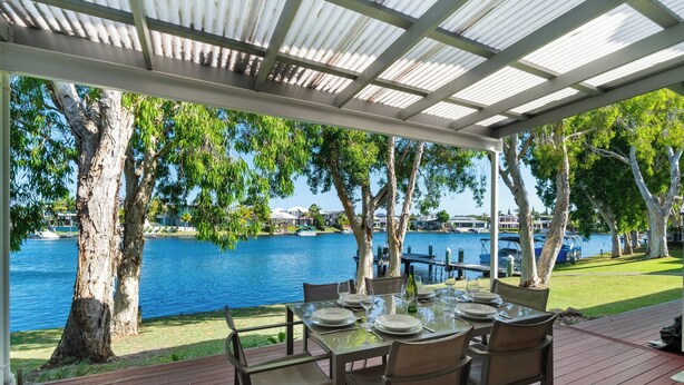 Un espace extérieur aménagé pour les repas, offrant une vue sur un lac et des bateaux, et entouré d’arbres et d’une terrasse couverte.