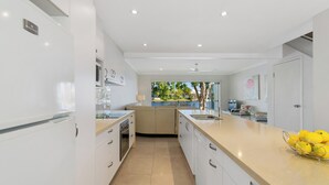 Une cuisine moderne avec des meubles blancs, un plan de travail beige et une vue sur un jardin.