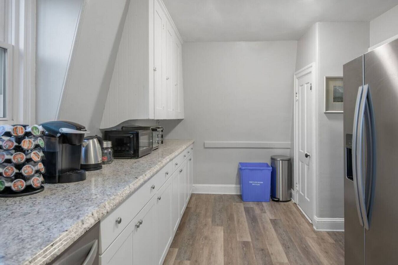 A compact kitchen with white cabinets, a stainless steel refrigerator, a microwave, and a coffee maker on the countertop.
