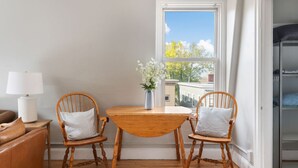 Una habitación acogedora con una mesa de madera y dos sillas, una ventana con vistas a edificios, y una puerta que da a un armario.