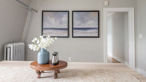 Una habitación con un radiador, un florero con flores y dos cuadros en la pared.