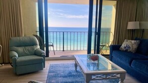 Een kamer met uitzicht op de oceaan, een blauwe bank, een glazen salontafel en een blauwe fauteuil.