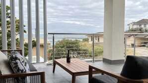 Un balcon avec une table en bois et deux chaises, donnant sur un quartier résidentiel et un plan d’eau.