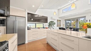 Une cuisine moderne dotée d’un grand îlot central, d’appareils électroménagers en acier inoxydable et offrant une vue sur l’extérieur.
