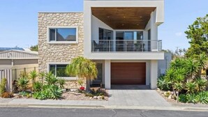 Une maison moderne à deux étages, dotée d’une façade en pierre, d’un balcon en bois et d’un garage.