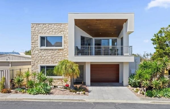 Une maison moderne à deux étages, dotée d’une façade en pierre, d’un balcon en bois et d’un garage.