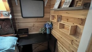 Ein kleiner Raum mit Holzwänden, einem Schreibtisch, Regalen und einem aufgehängten Bilderrahmen.